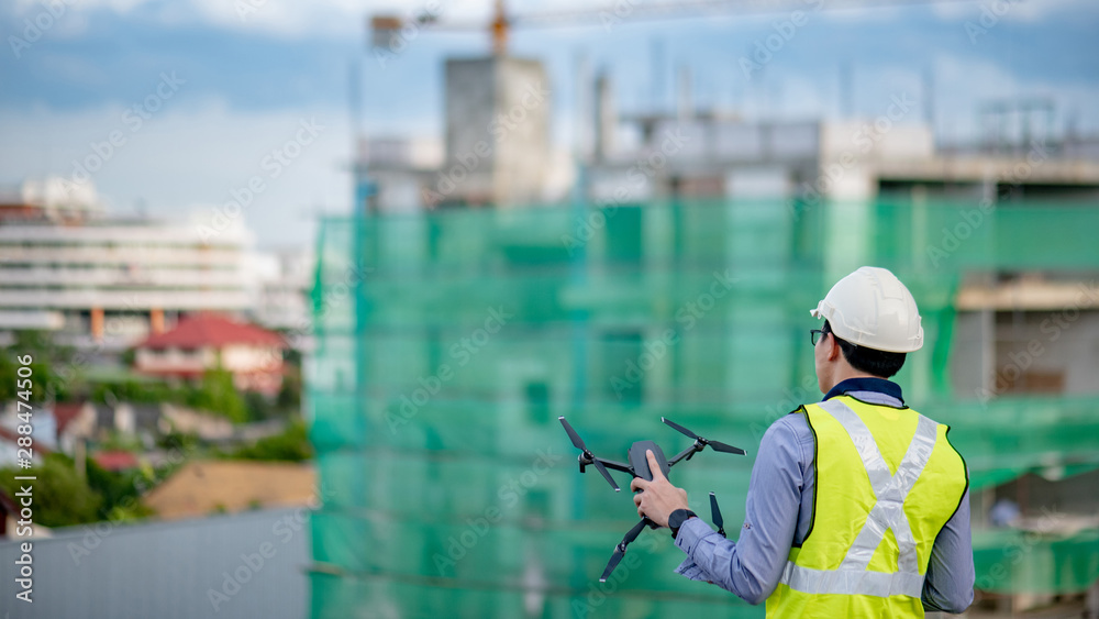 Wall mural asian engineer man holding drone at construction site. male worker using unmanned aerial vehicle (ua