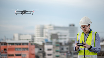 Asian engineer man flying drone over construction site. Male worker using unmanned aerial vehicle (UAV) for land and building site survey in civil engineering project.