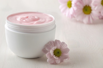 Fototapeta na wymiar Cream. cosmetics for face and body. Pink cream and flower in a white jar on a white wooden table