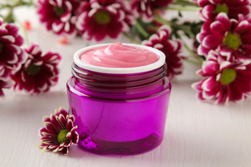 Obraz na płótnie Canvas Cream. cosmetics for face and body. Pink cream and flower in a purple jar on a white wooden table.
