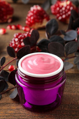 Fototapeta na wymiar Cream. cosmetics for face and body. Pink cream and flowering branches and pomegranate in a purple jar on a brown wooden table.