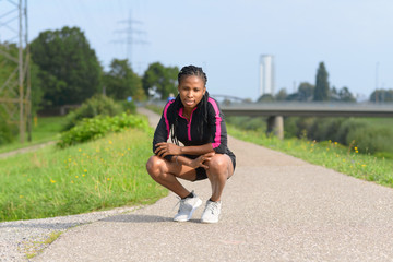 Fit sporty African woman crouching on a rural road