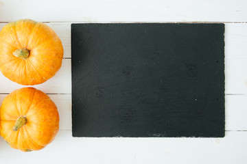 Orange pumpkins on wite wooden background and black slate stone surface. Thanksgiving and Halloween...