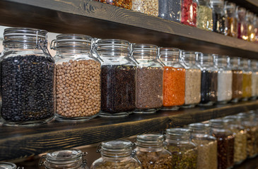 Health Food Ingredients - herbs, seeds and pulses in spice jars, with reflections - lentils, split peas, pearl barley, coriander seed, black pepper, cous cous, corn, and rice - panorama.