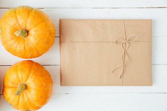 Autumn orange pumpkins with gift in brown paper package tied up with strings on old white wooden background Thanksgiving and Halloween concept. Top view. Copy space for text and design
