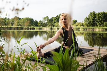 Kobieta ćwiczy jogę na drewnianym pomoście nad jeziorem. Joga na świeżym powietrzu. Kobieta...