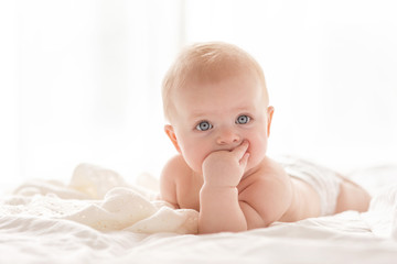 Happy little baby girl infant on a bed in white bedroom near the bright window