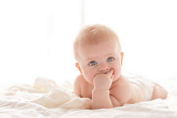 Happy little baby girl infant on a bed in white bedroom near the bright window
