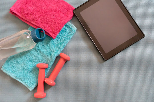 Feminine exercise & fitness equipment and digital tablet. Athletics tools for exercise at home and rehab. Muscle class training. Towel and hydration flat lay