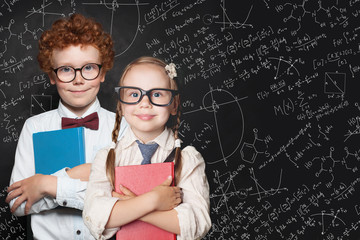 Smart kids portrait. Little girl and boy student holding books and standing against blackboard...