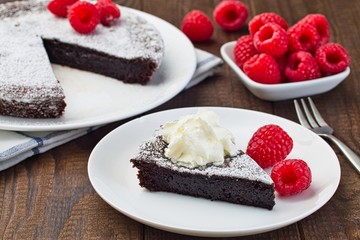 Piece of chocolate sticky brownie cake, swedish dessert Kladdkaka, on plate, garnished with icing sugar, whipping cream and raspberry, horizontal
