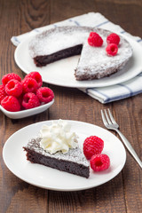Piece of chocolate sticky brownie cake, swedish dessert Kladdkaka, on plate, garnished with icing sugar, whipping cream and raspberry, vertical