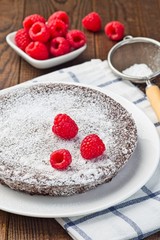 Chocolate sticky brownie cake, swedish dessert Kladdkaka, on a plate, garnished with icing sugar and raspberry, vertical
