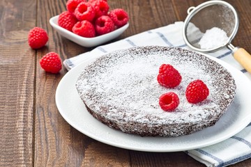 Chocolate sticky brownie cake, swedish dessert Kladdkaka, on a plate, garnished with icing sugar and raspberry, horizontal