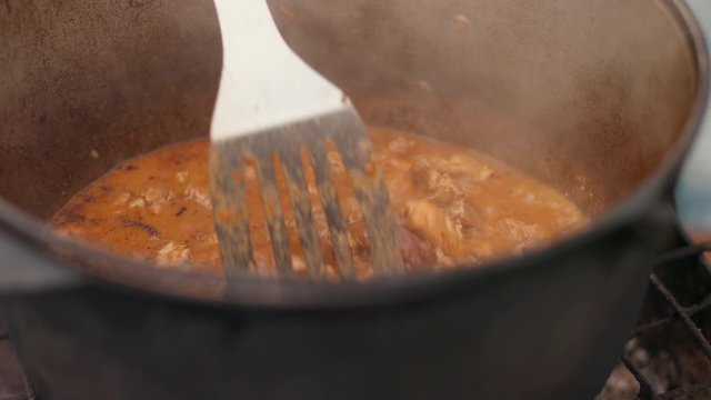 in large cast iron pot preparing dish, red with meat onions and other components