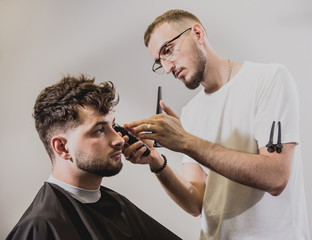 Young man with trendy haircut at barber shop. Barber does the hairstyle and beard trim.