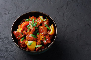 Chicken Manchurian in bowl at black concrete background. Chicken Manchurian is Indian Chinese cuisine dish with Chicken breasts, bell pepper, tomatoes, soy sauce. Copy space