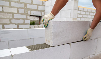 A worker lays foam concrete bricks in a house under construction - obrazy, fototapety, plakaty