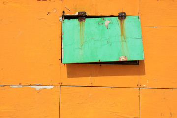 Close up old peeled yellow and green colored wooden wall and window detail of building exterior