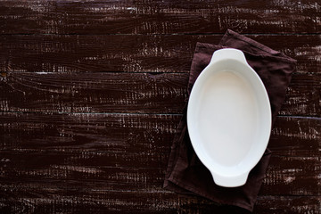 Ceramic white baking dish on a wooden old background.