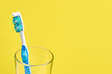 Colorful toothbrush in a glass. Oral hygiene concept. Yellow background. Copy space in the right.