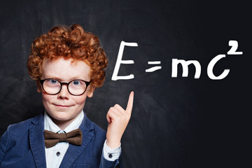 Confident child student on blackboard background pointing at science formula
