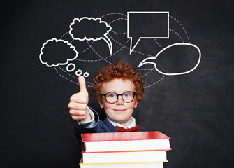 Happy little boy and blank speech clouds bubbles. Smart kid in glasses on school blackboard background