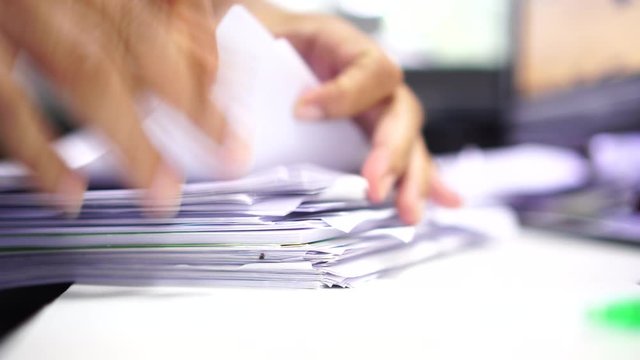 Businessman hands working in stacks of paper files for searching information on work desk office, business report papers,piles of unfinished documents achieves