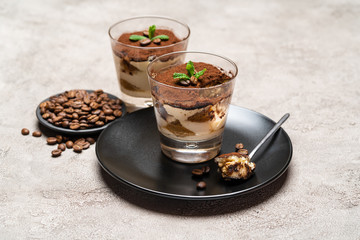 Portion of Classic tiramisu dessert in a glass cup on concrete background