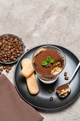 Portion of Classic tiramisu dessert in a glass cup on concrete background