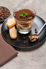 Portion of Classic tiramisu dessert in a glass cup on concrete background