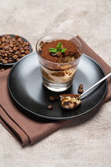 Portion of Classic tiramisu dessert in a glass cup on concrete background