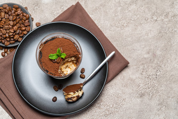 Portion of Classic tiramisu dessert in a glass cup on concrete background