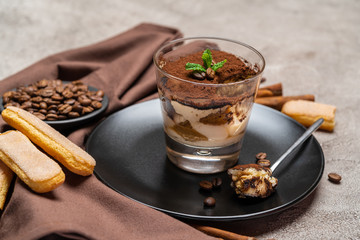 Portion of Classic tiramisu dessert in a glass cup on concrete background