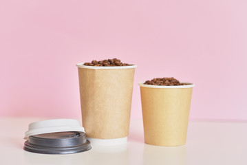 Two paper coffee cups with coffee beans on pink background