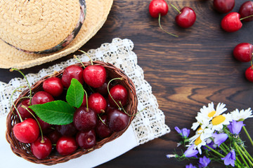 Red Cherries and summer straw hat on brown wooden table.