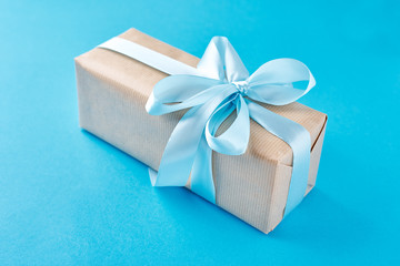 close up gift box in craft paper with blue ribbon on a blue background