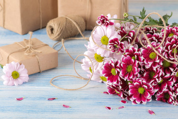 Bouquet of autumn flowers of pink chrysanthemums and gift boxes on a blue wooden table.