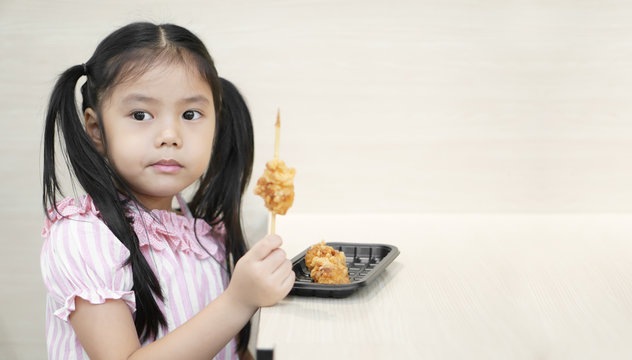 Asian Child Hungry Or Kid Girl Enjoy Eating Fried Chicken Food Or Meat Ball Skewers But Careful Of Dangers Of Sharp Wood For Delicious And Happy Smile For Lunch Or Breakfast At Food Court Restaurant