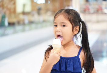 Asian child cute or kid girl happy and enjoy eating or lick ice cream cone delicious and yummy for sweet dessert or snack and cold refresh with fulfill on summer holiday at department store