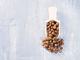 Allspice (Jamaica pepper) in wooden scoop on a gray background with stains