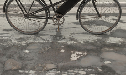 Fototapeta na wymiar Old retro bicycle on wet cracked asphalt with pits and puddles on a cloudy rainy day. 3D rendering illustration.