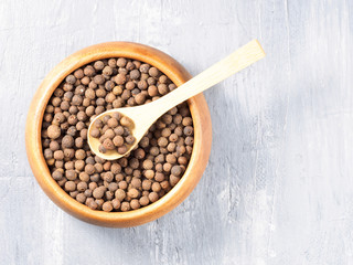 Allspice (Jamaica pepper) in a wooden cup and spoon on a gray background