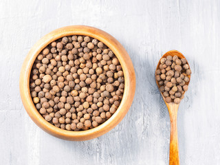 Allspice (Jamaica pepper) in a wooden cup and spoon on a gray background