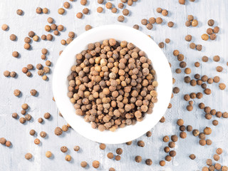 Allspice (Jamaica pepper) in a white cup on a gray background