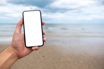 Mockup image of a hand holding and showing black mobile phone with blank desktop screen on the beach
