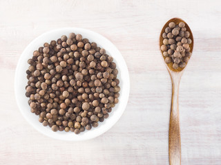 Allspice (Jamaica pepper) in a white cup and spoon on a brown wooden background
