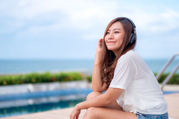 A beautiful asian woman listening to music  with headphone while sitting by swimming pool