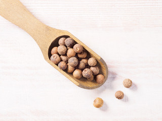 Allspice (Jamaica pepper) in a wooden scoop on a brown wooden background diagonally