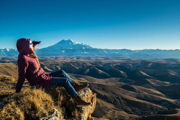 Fototapeta premium Beautiful young woman in front of gorgeous mountain Elbrus during sunny autumn day, landscape form plateau Bermamyt
